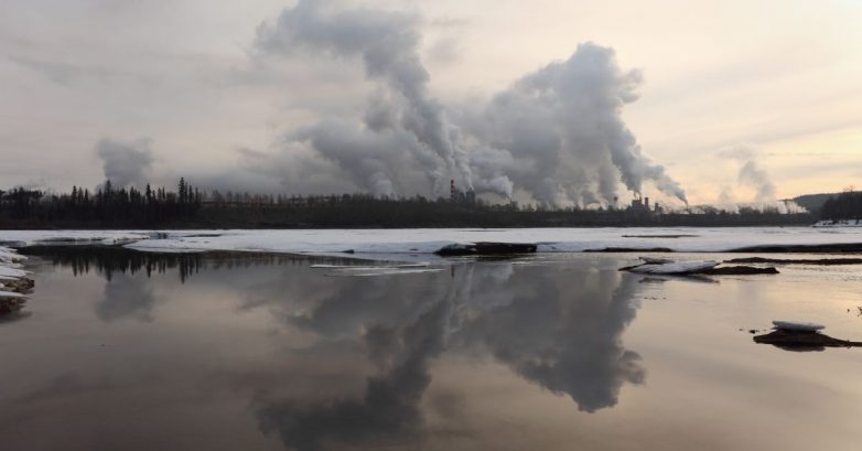 Factory smokestacks emitting heavy smoke over river
