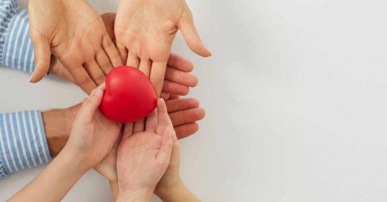 Multiple hands holding red heart symbol together