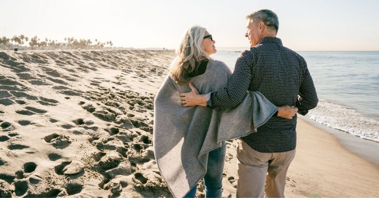 Older couple walking arm in arm on beach
