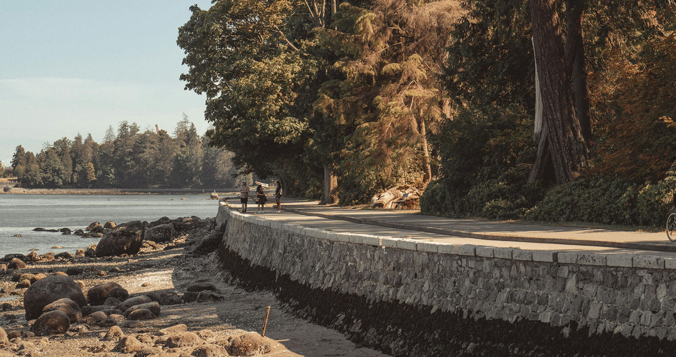 People walking along waterfront path beside rocky shore