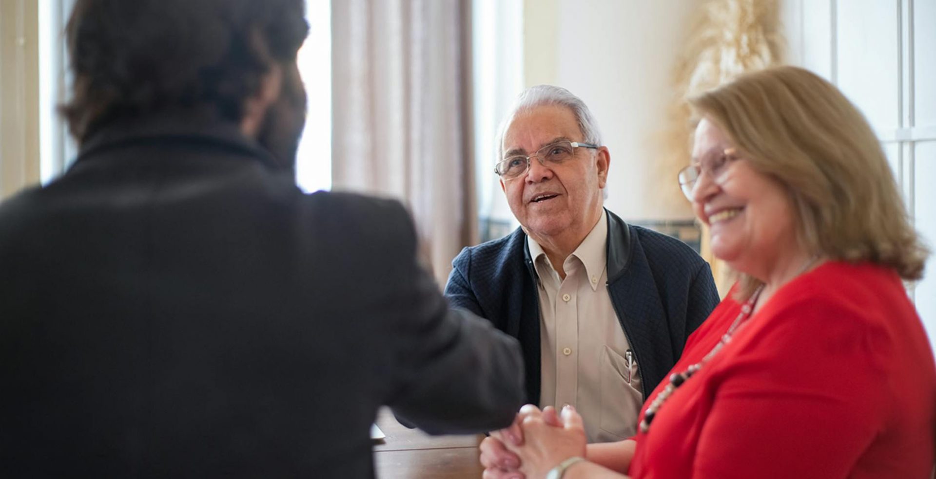 Senior couple meeting financial advisor, shaking hands indoors
